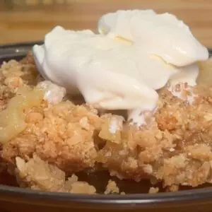 Homemade apple crumble with ice cream on a plate, showcasing a delicious dessert with a crunchy topping.